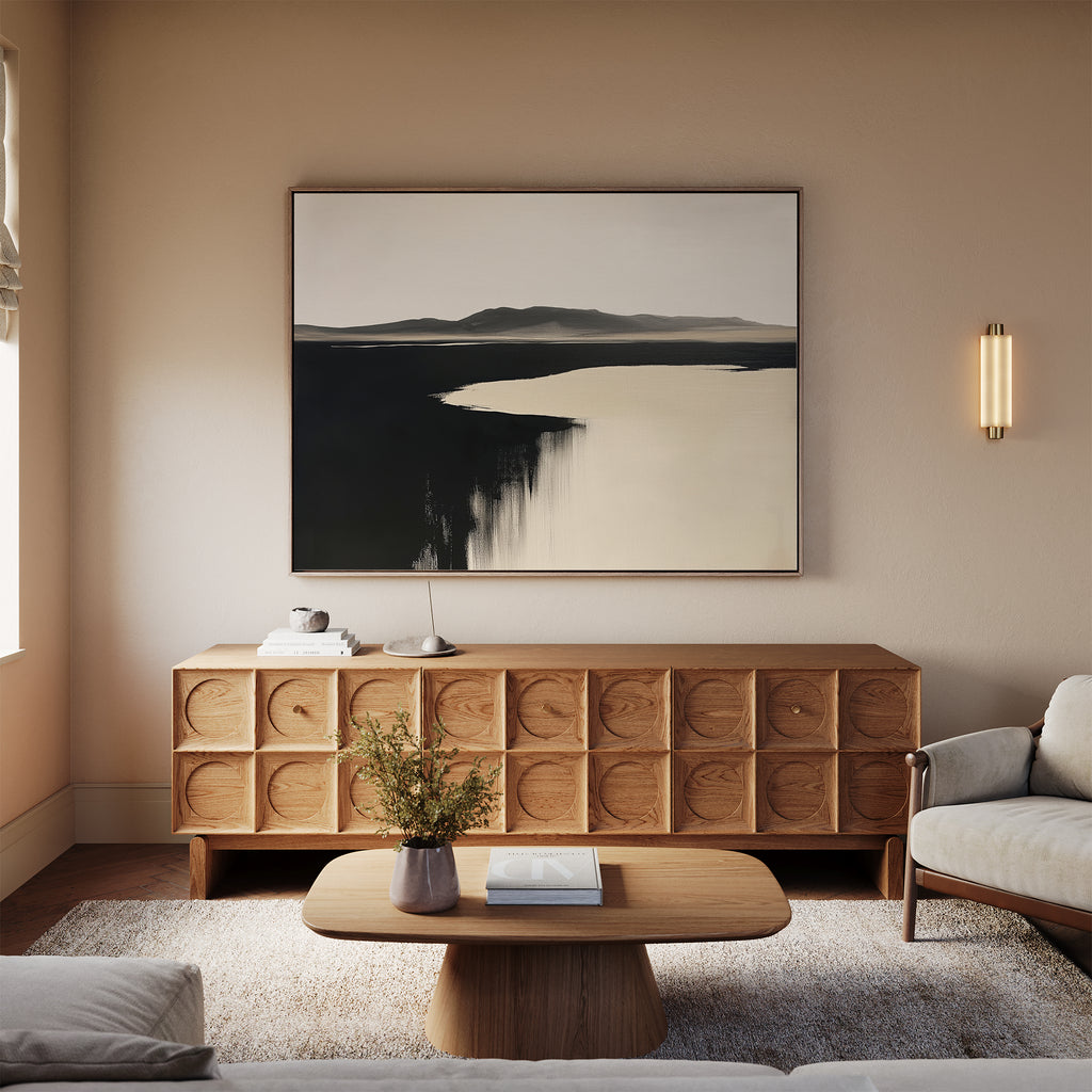 A modern living room with a light beige sofa, wooden coffee table, carved sideboard, and Black Shore Canvas Art – Horizontal; neutral tones and minimal decor create a calm, inviting space.