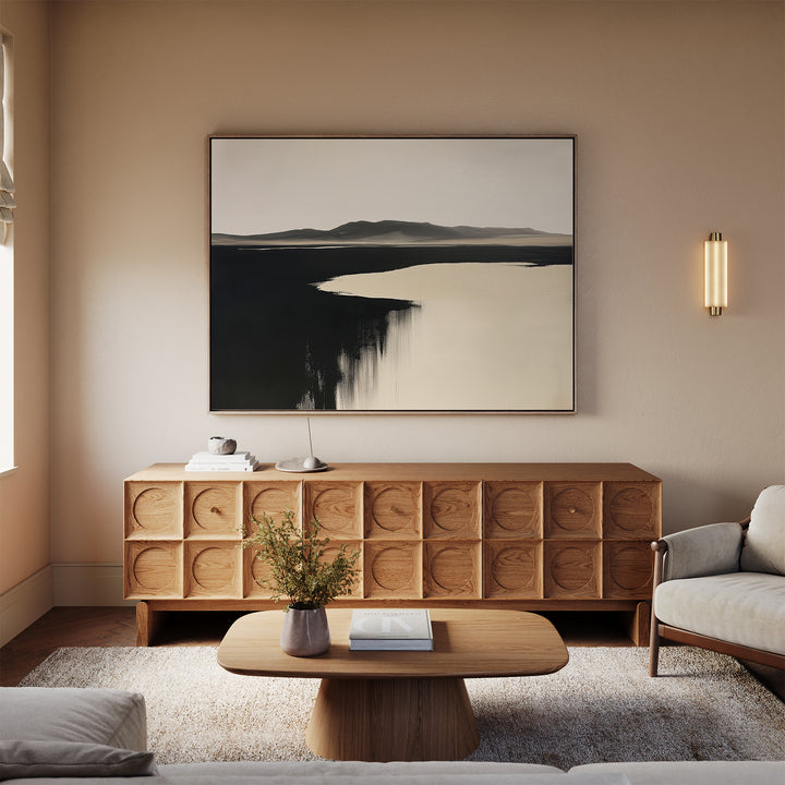 A modern living room with a light beige sofa, wooden coffee table, carved sideboard, and Black Shore Canvas Art – Horizontal; neutral tones and minimal decor create a calm, inviting space.