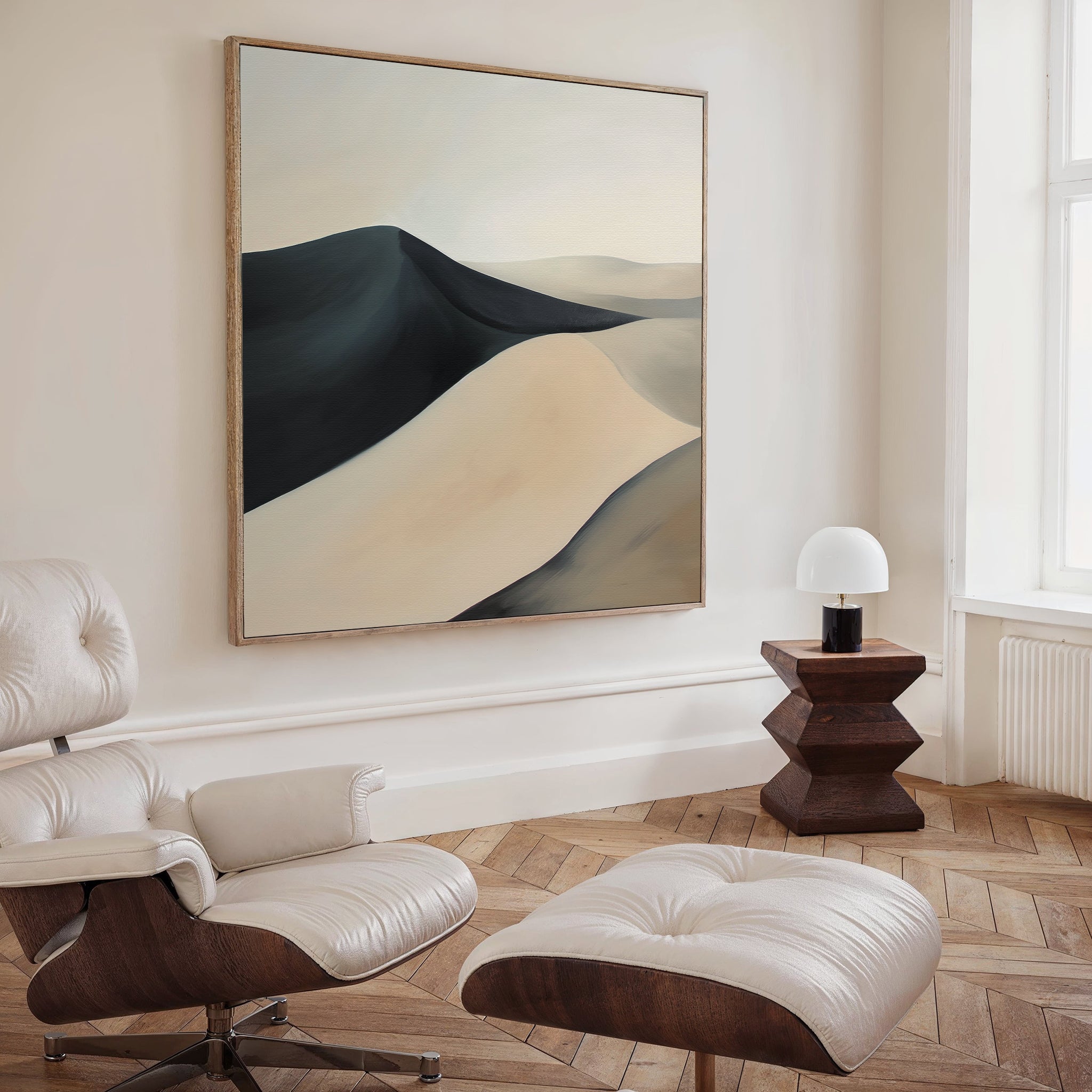 A modern living room with a white leather chair and ottoman, wooden side table with lamp, and the Black Veil Abstract Canvas Art in neutral tones. Light walls and herringbone wood flooring complete the elegant decor.