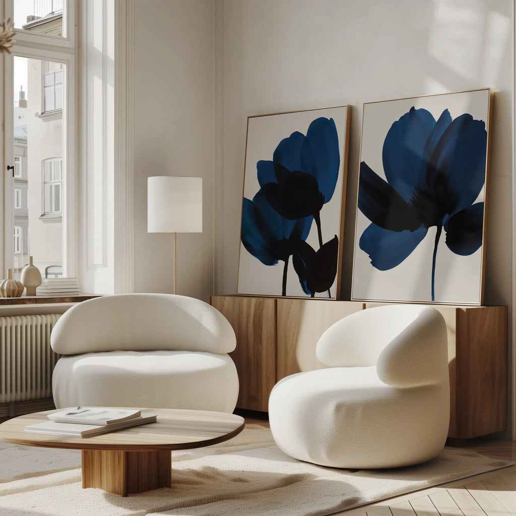 A modern living room featuring the Bloom Set of 2 white, rounded chairs, a low wooden coffee table, abstract blue floral wall art, a floor lamp, and sunlight streaming through tall windows—perfect for relaxing in Nordic Park style.