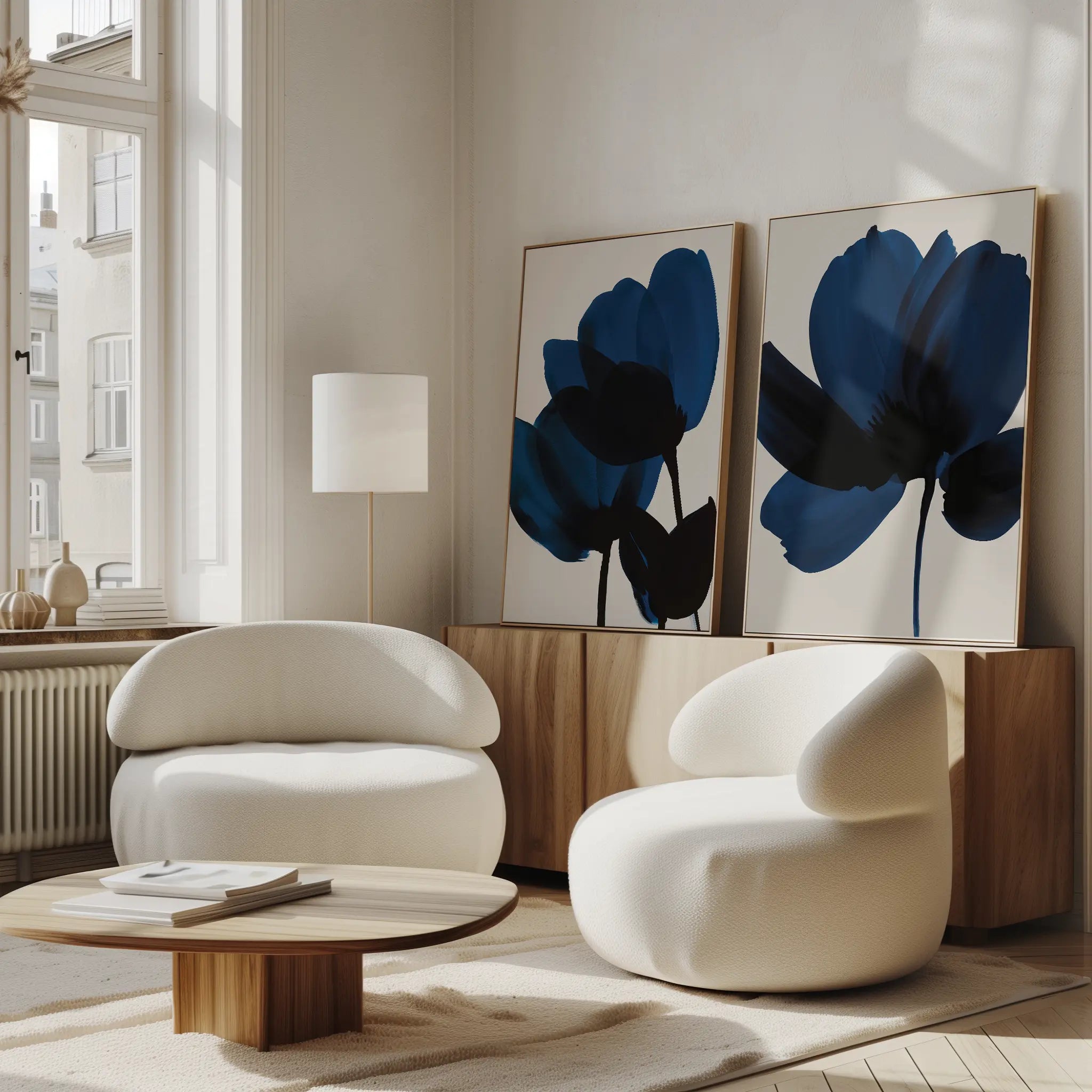 A modern living room featuring the Bloom Set of 2 white, rounded chairs, a low wooden coffee table, abstract blue floral wall art, a floor lamp, and sunlight streaming through tall windows—perfect for relaxing in Nordic Park style.