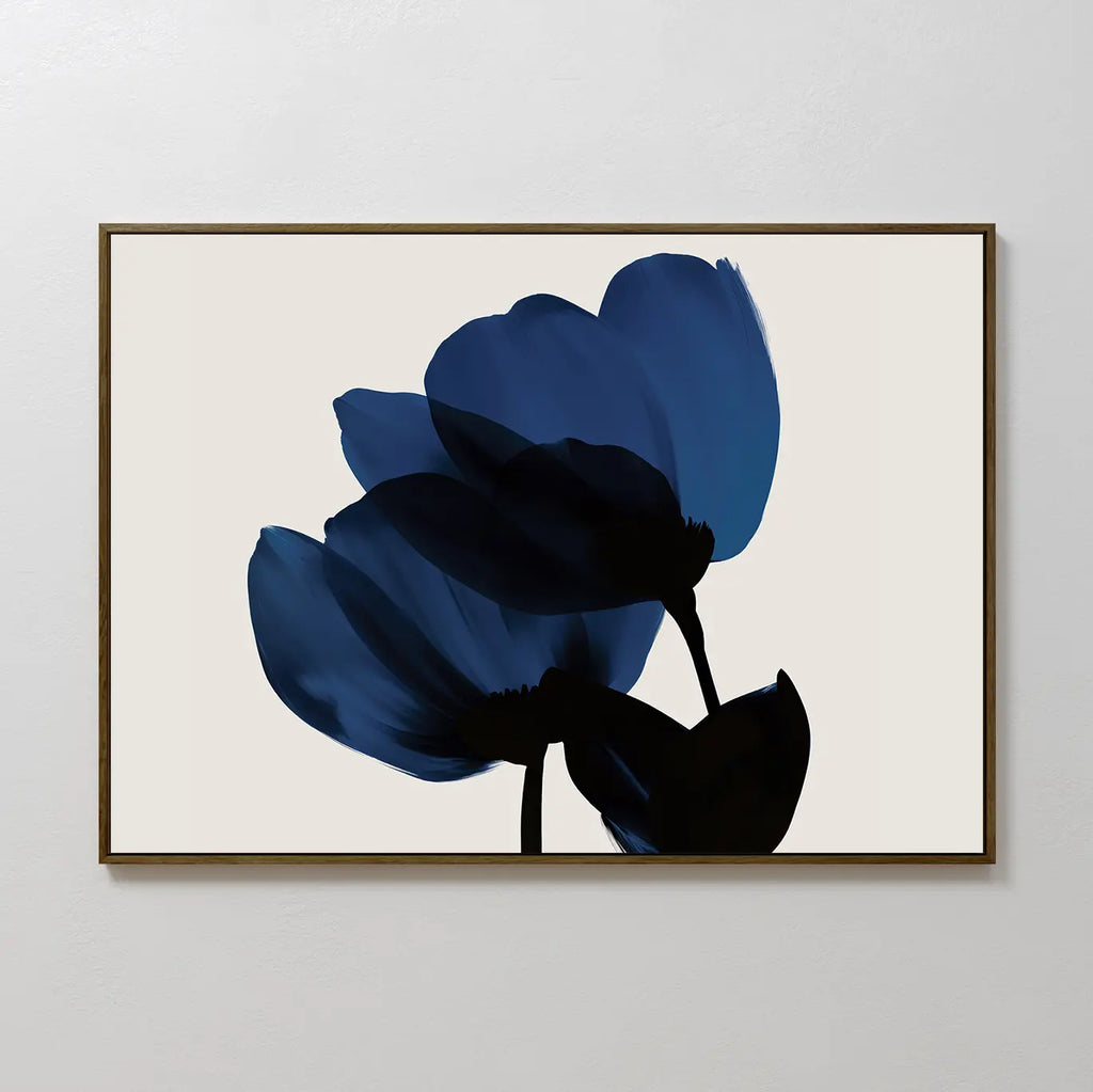 The Bloom Abstract Canvas Art – Horizontal displays two large, abstract blue flowers with black stems and leaves on a light beige background, set in a thin dark wood frame—ideal for modern living room decor.