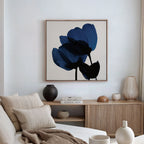A modern living room with a beige sofa, neutral cushions, wooden sideboard, decorative vases, books, and the Bloom Abstract Canvas Art – Square featuring abstract blue flowers on a white wall.