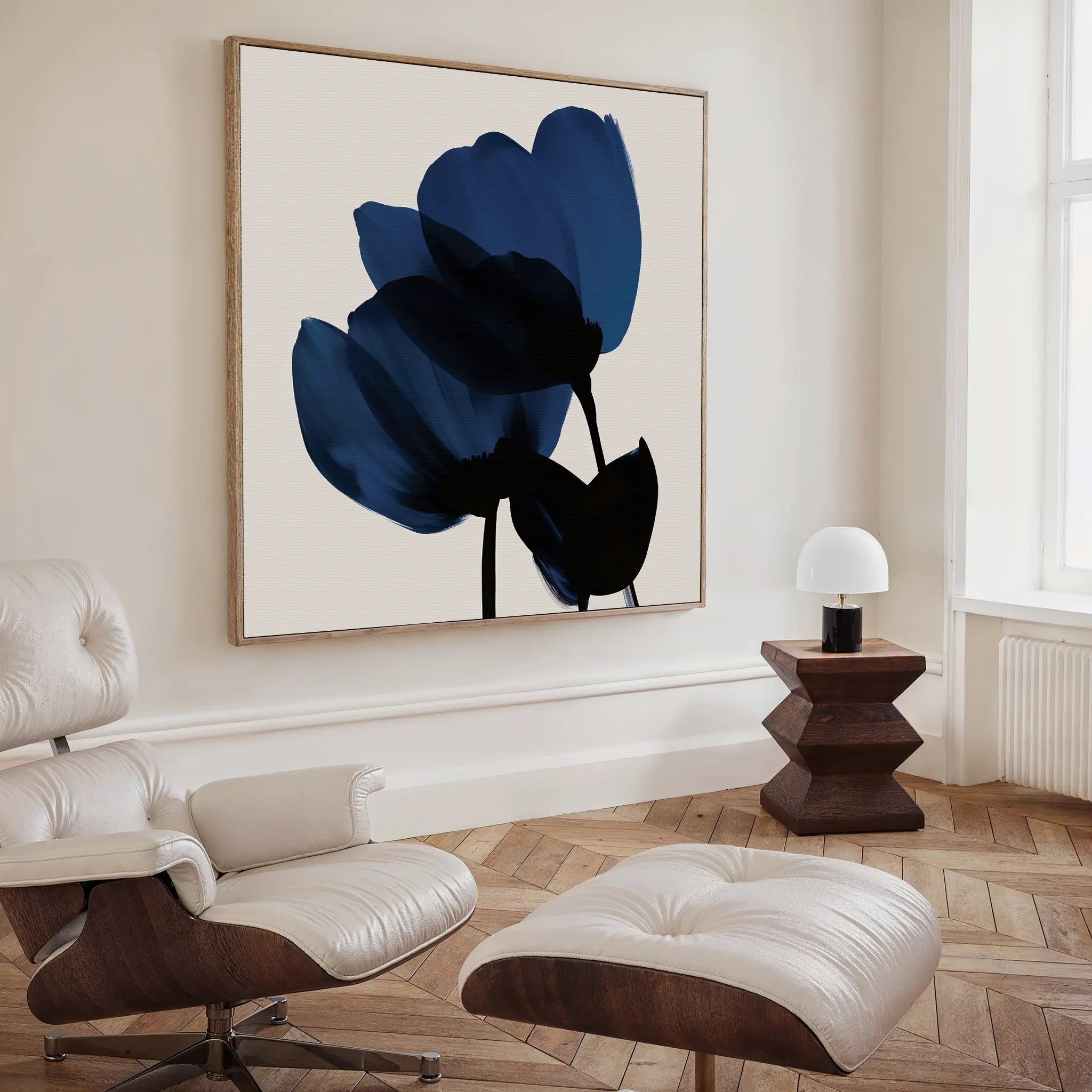 A modern living room with a white lounge chair and ottoman, dark wood side table, herringbone floors, and the Bloom Abstract Canvas Art – Square brings bold, contemporary flair to the space.