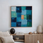 A modern living room showcases Blue Mosaic Abstract Canvas Art with blue and teal blocks, a beige sofa, and a wooden sideboard adorned with vases, a bowl, and stacked travel books.
