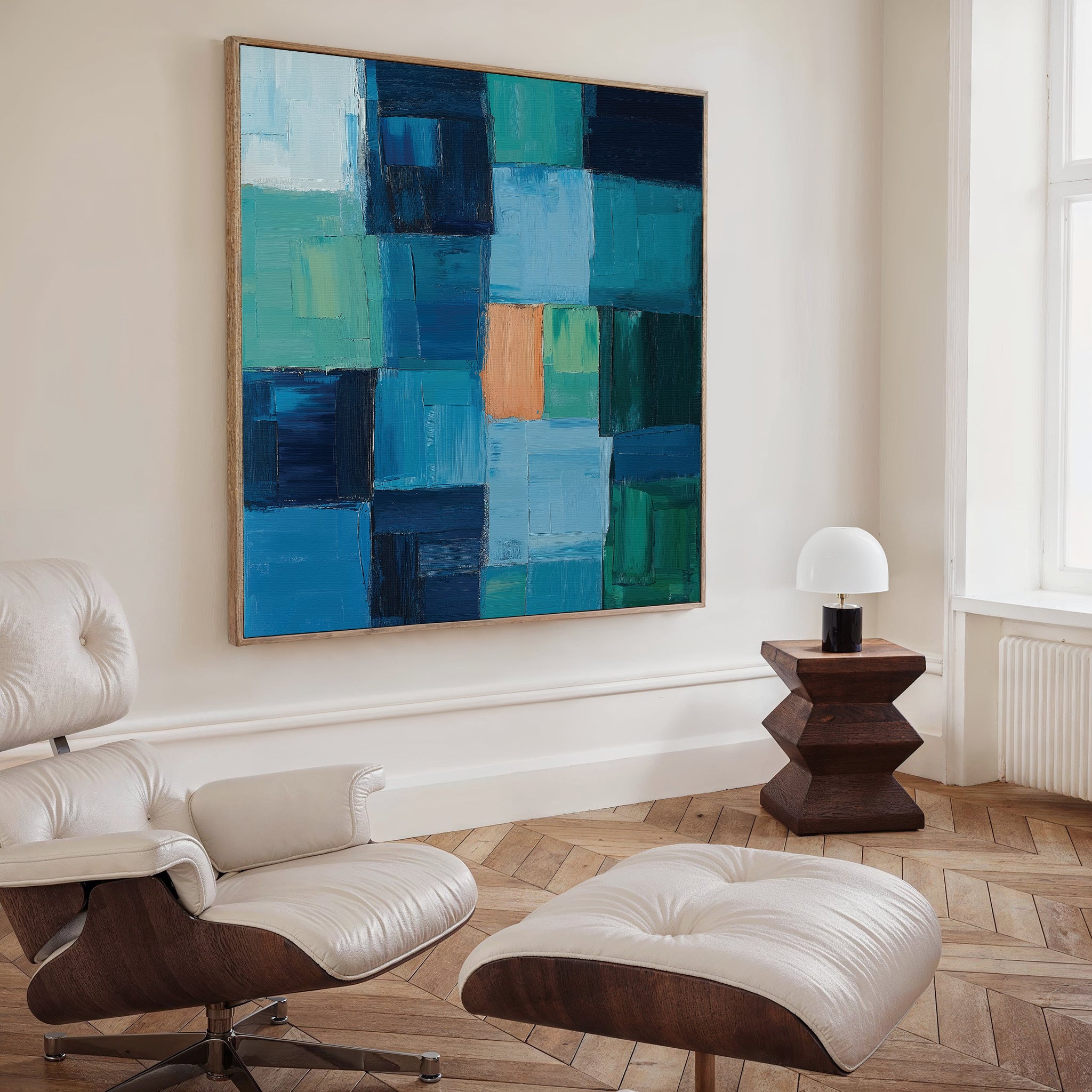 A modern living room with a white lounge chair, ottoman, wooden side table with a white lamp, and the Blue Mosaic Abstract Canvas Art featuring vibrant blue, green, and orange blocks as a striking decor piece.