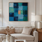 A modern living room with a beige sofa, light cushions, a side table with a white lamp, a vase of dried flowers, and Blue Mosaic Abstract Canvas Art featuring blue and green squares as the focal point of the decor.