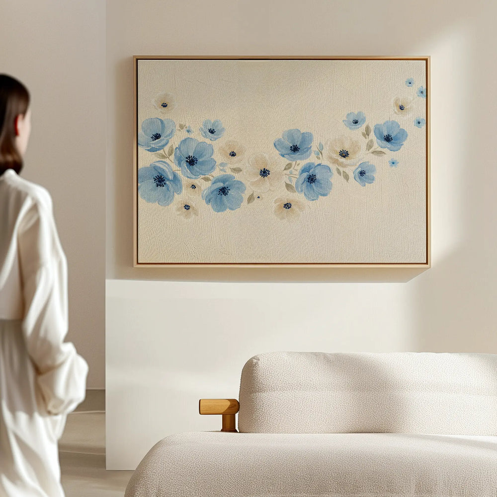 A person stands in a minimal, light-filled room with a beige sofa and Blue Prairie Canvas Art—a large piece featuring blue flowers on a cream background, adding the perfect minimalist canvas style.