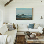 A bright, cozy living room with white shiplap walls, a spacious white sectional sofa, a rustic wooden coffee table, and tranquil Blue Ridge View Canvas Art featuring misty blue mountains displayed on the wall.