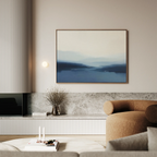 A modern living room features the Blue Valley Mist Canvas Art above a marble shelf, a curved brown sofa, a round light fixture, and minimalist decor like a vase with dried branches on the shelf.