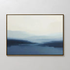 Blue Valley Mist Canvas Art features soft, blurred layers of blue and white, evoking a misty seascape. Framed in brown and ideal for minimalist decor, it adds serene landscape style when displayed on a plain white wall.