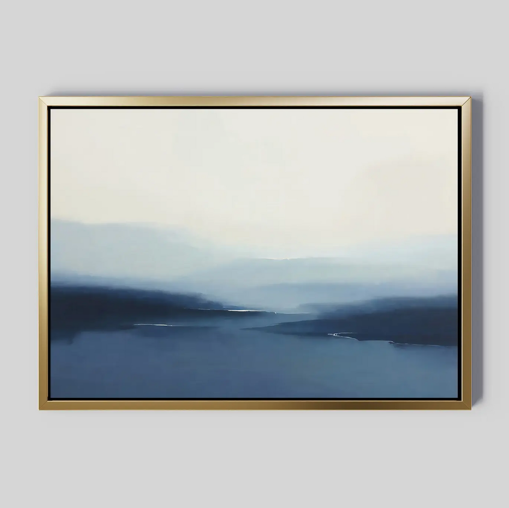 Blue Valley Mist Canvas Art features abstract blue and white tones evoking a misty landscape, with soft, blended edges. Framed in simple gold and set on a light gray background, it’s perfect for minimalist décor.