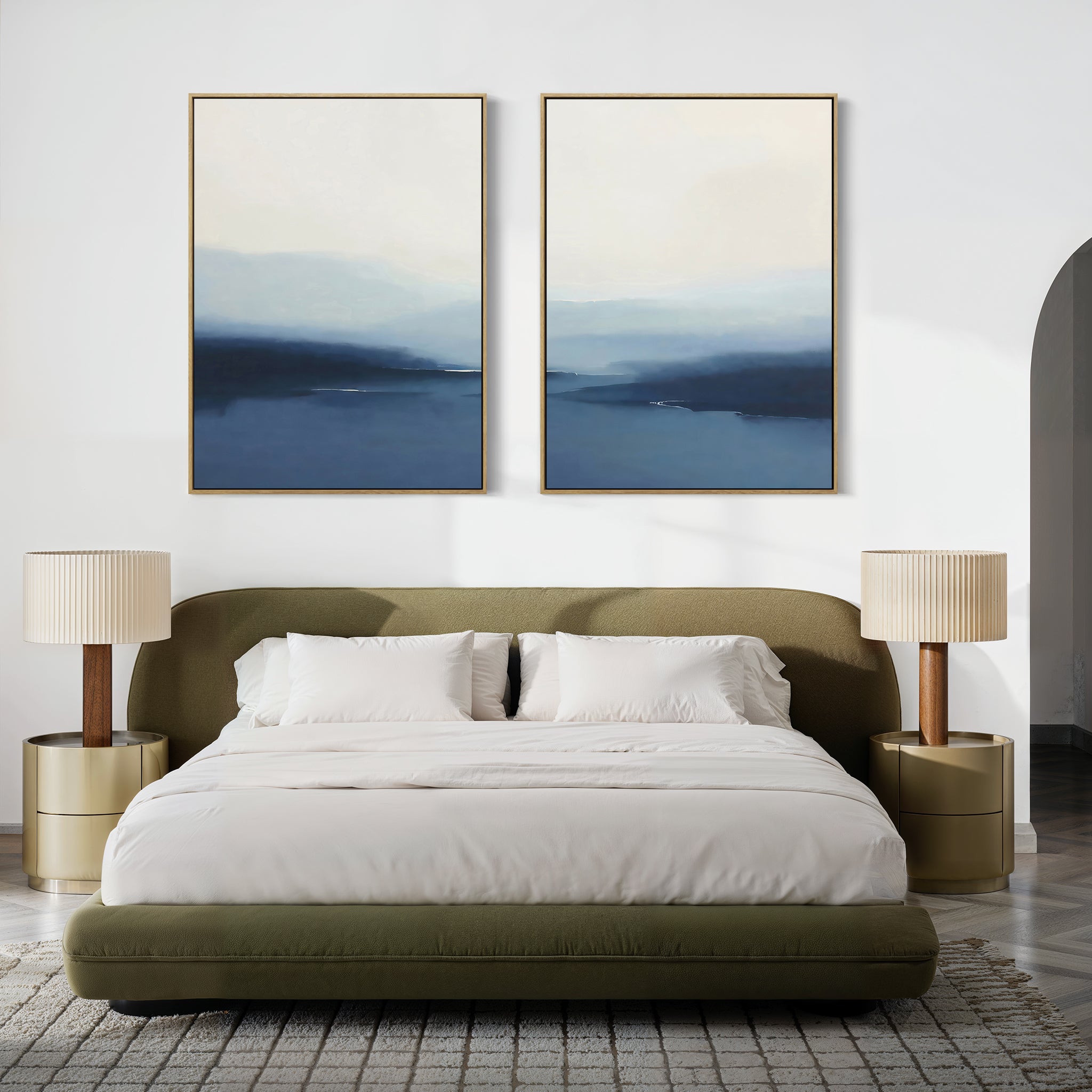 A modern bedroom with a low olive-green bed, white bedding, minimalist decor, two gold nightstands with beige lamps, and the Blue Valley Mist Set of 2 wall art above the bed. A gray rug covers the wooden floor.
