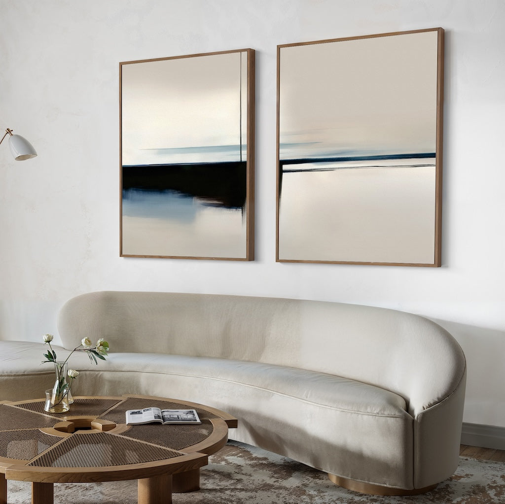A modern living room with a curved beige sofa, a round wooden coffee table topped with a single flower in a vase, and the Blurred Reflections Set of 2 large minimalist wall art prints in neutral tones hanging above the sofa.