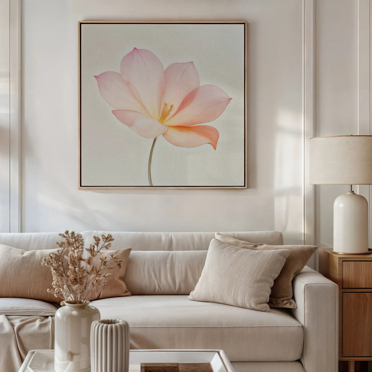A modern living room featuring a white sofa with beige cushions, side table and lamp, dried flowers in a vase, and the Blush Magnolia Canvas Art—an eye-catching large pink floral painting—hanging above the sofa.
