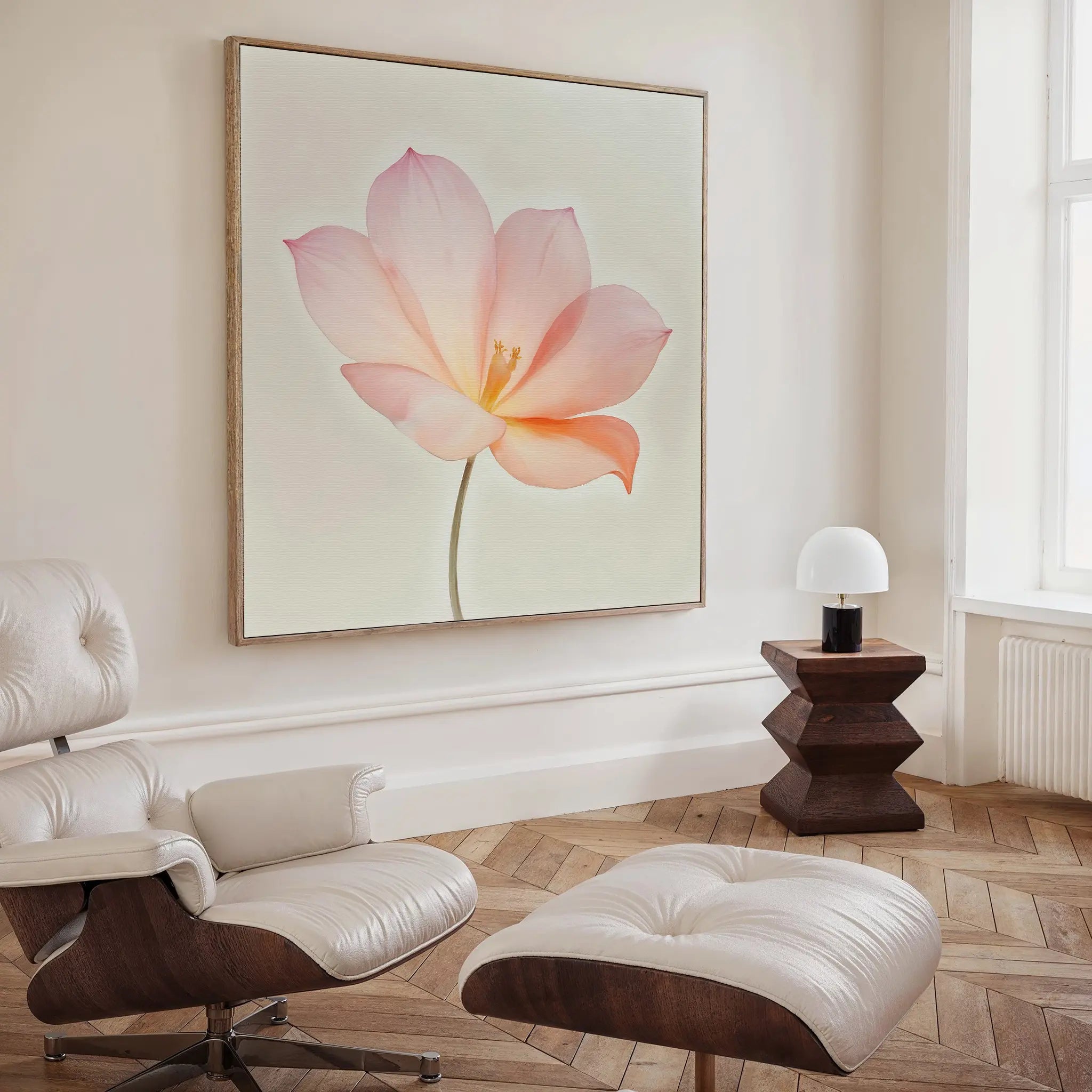 A modern, minimalist living room featuring a white leather lounge chair with ottoman, a wooden side table with a small white lamp, and the Blush Magnolia Canvas Art as a striking centerpiece.