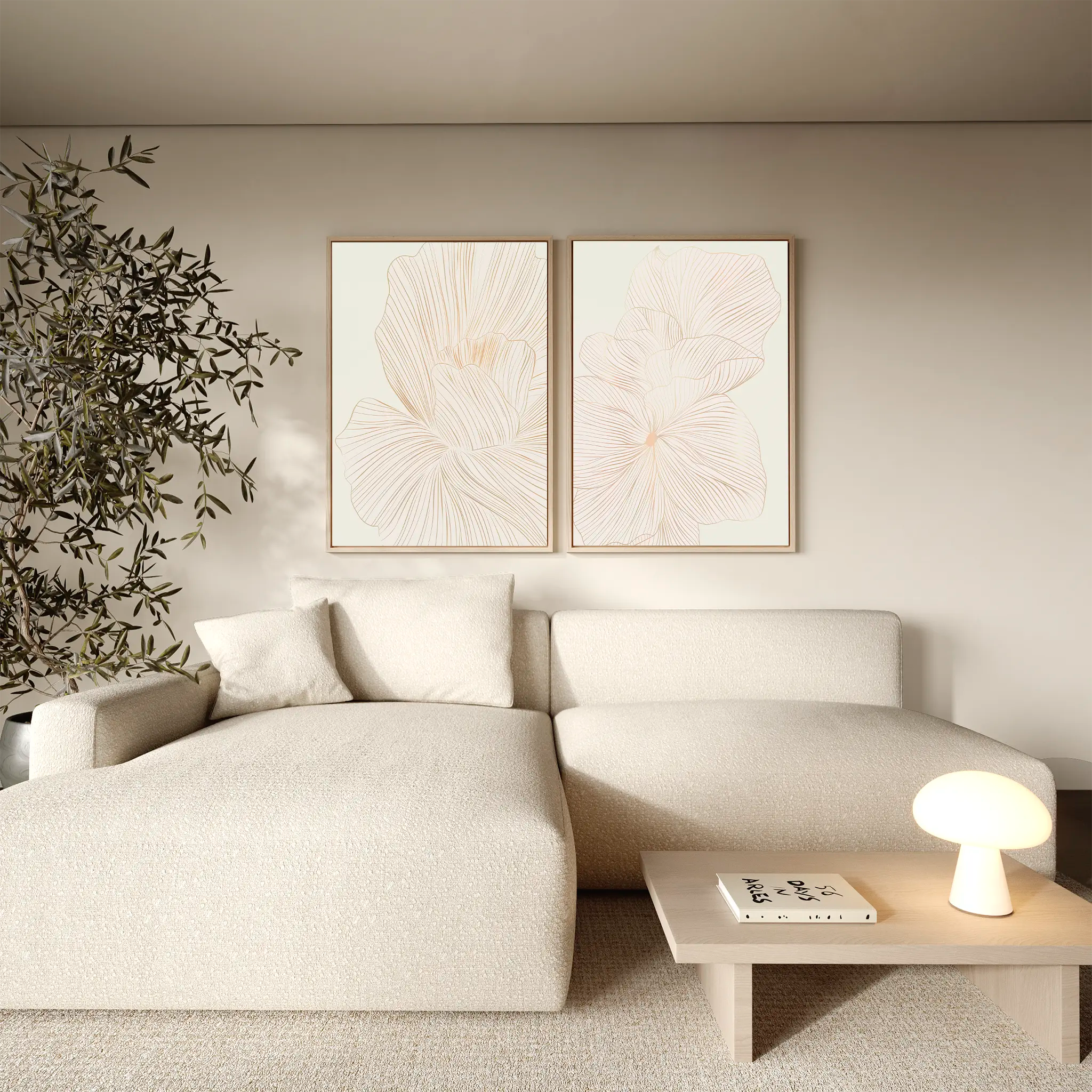 A modern living room with a light beige sectional sofa, a small wooden coffee table topped with books and a lit lamp, the Blush Sketch Set of 2 wall art prints on the wall, and a leafy potted plant in the corner.
