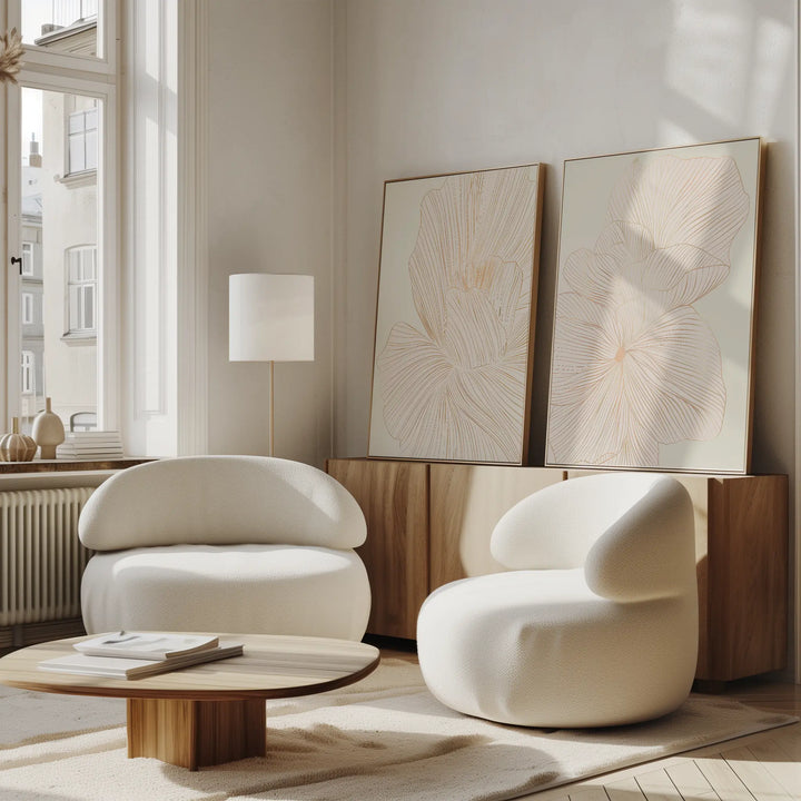 A modern living room featuring two curved white armchairs, a wooden coffee table, a light wood sideboard, minimalist lamp, and the Blush Sketch Set of 2 as wall art—all in soft, neutral tones.