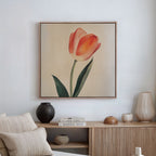 The Blush Tulip Canvas Art, showcasing an orange tulip with green leaves, is displayed above a wooden sideboard with vases and books. A beige sofa with striped cushions completes this modern minimalist decor.