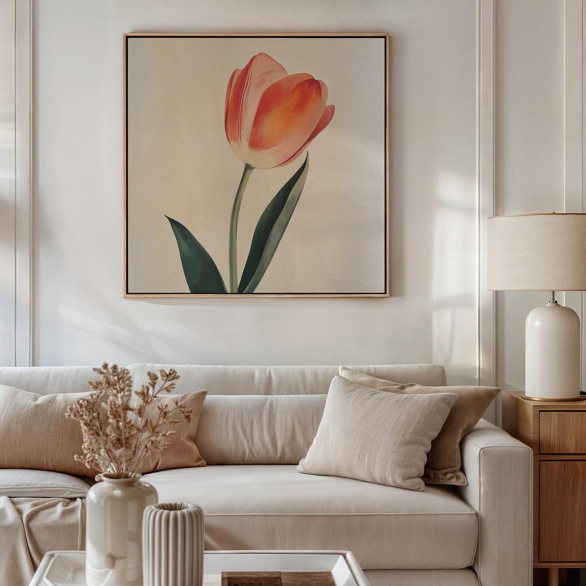 A modern living room with a beige sofa, neutral pillows, a side table with a lamp, and minimalist Blush Tulip Canvas Art on the wall. A vase with dried flowers sits on the coffee table in the foreground.