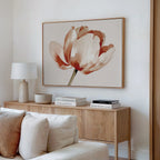 A modern living room with a light wood sideboard, white table lamp, decorative bowls, stacked books, and striking Blush Tulip Canvas Art featuring red and beige flowers above a cream-colored sofa.