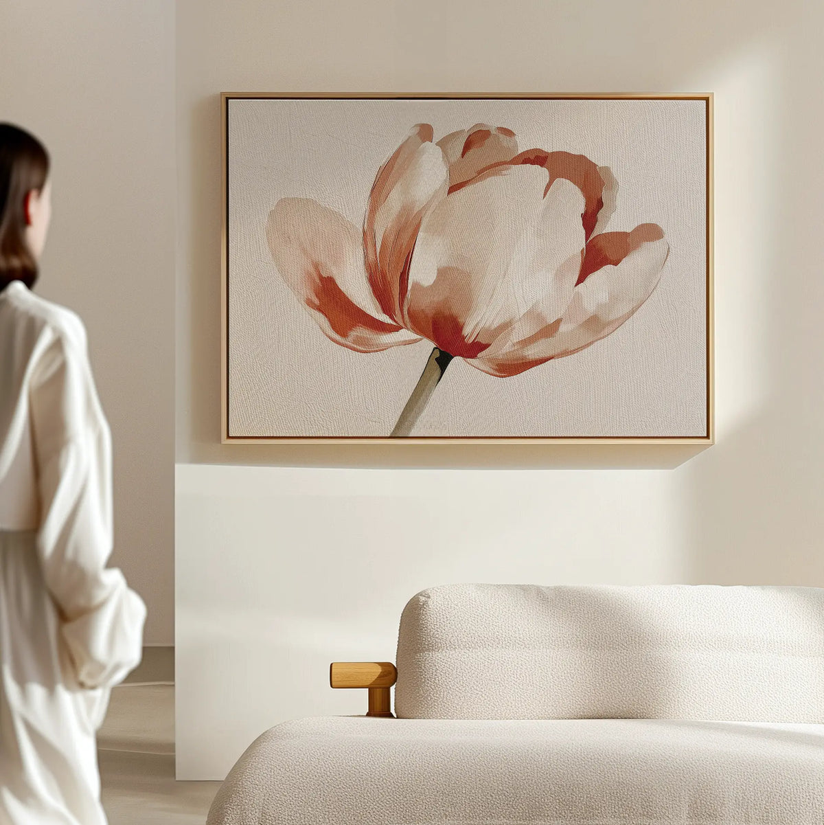 A person in white admires the Blush Tulip Canvas Art above a light sofa, adding elegance to a cream wall and softly lit, minimalistic room.