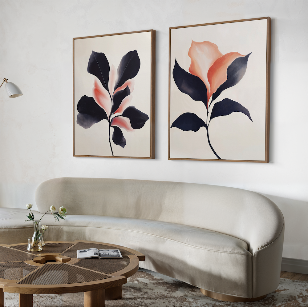 A modern living room with a curved beige sofa, a round wooden coffee table, and the Blush & Shadow Set of 2 large botanical art prints featuring abstract flowers displayed above the sofa.