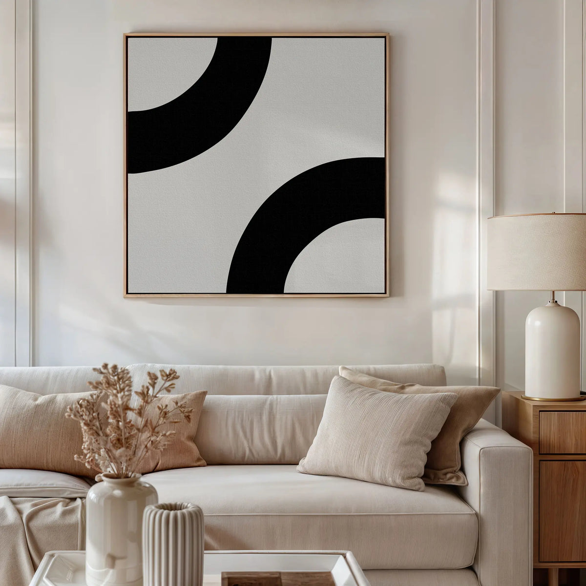 A modern living room with a beige sofa, neutral cushions, a wooden side table with a white lamp, dried flowers in a vase, and Bold Orbit Canvas Art as minimalist wall décor.