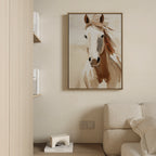 The Bold Spirit Canvas Art, a framed minimalist horse artwork, hangs above a cream sofa on a beige wall. Nearby shelves display books, while a small decorative object on the floor completes the living room decor.