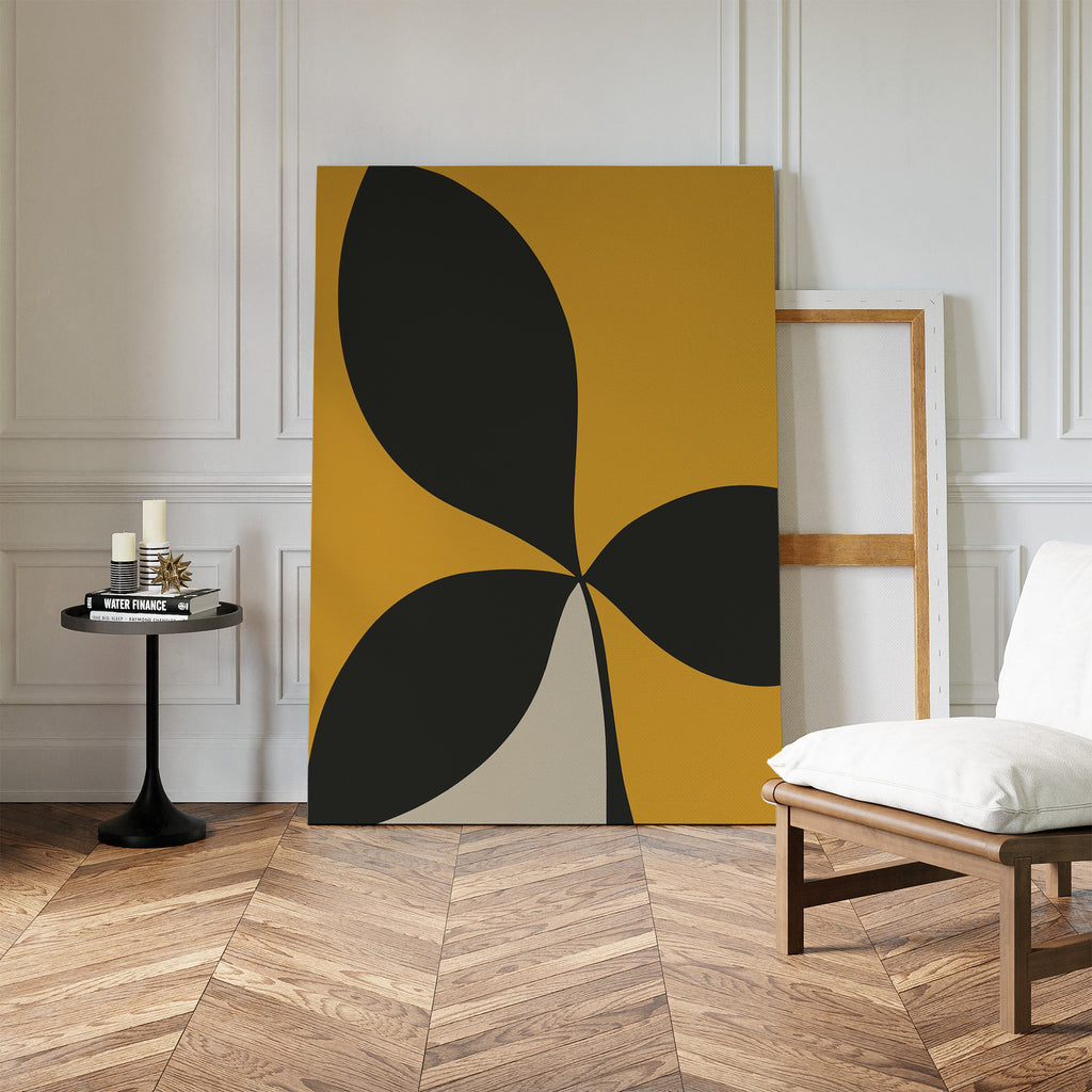 A modern interior with herringbone wood flooring, a white cushioned chair, and a round black side table with candles is highlighted by minimalist wall art—the Botanic Contrast Abstract Canvas Art in bold black and beige on mustard yellow.