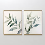 The Botanical Breeze Set of 2 features framed watercolor paintings of leafy branches in soft green and blue, displayed side by side. This minimalist wall art set brings a touch of nature to your decor.