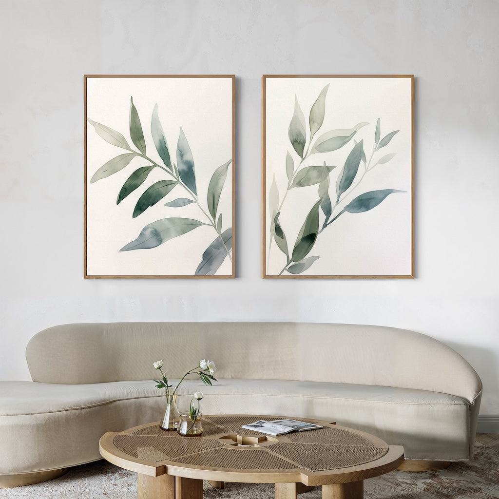 Minimalist living room with a curved beige sofa, round wooden coffee table with a glass vase of white flowers, and the Botanical Breeze Set of 2 wall art prints displayed on a light-colored wall.