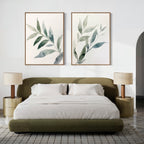 A modern bedroom with a low olive-green bed, white bedding, two beige nightstands with matching lamps, and the Botanical Breeze Set of 2 minimalist wall art above the bed. The space features neutral tones and a textured rug.
