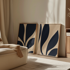 The Botanical Ink Set of 2, featuring framed abstract modern wall art in navy blue and beige, is displayed leaning against a light wall in a cozy, sunlit room with a cream sofa and minimalist decor.