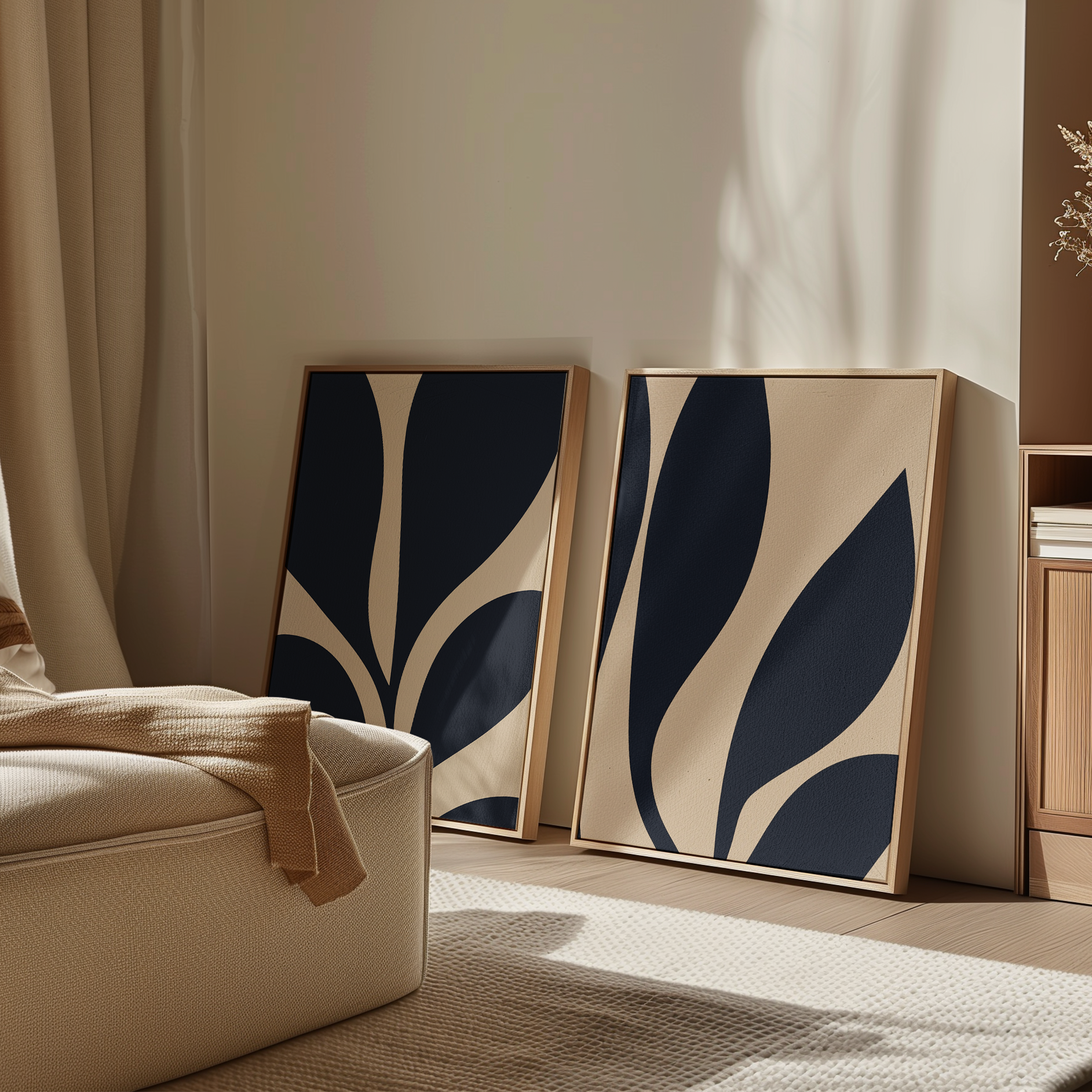 The Botanical Ink Set of 2, featuring framed abstract modern wall art in navy blue and beige, is displayed leaning against a light wall in a cozy, sunlit room with a cream sofa and minimalist decor.