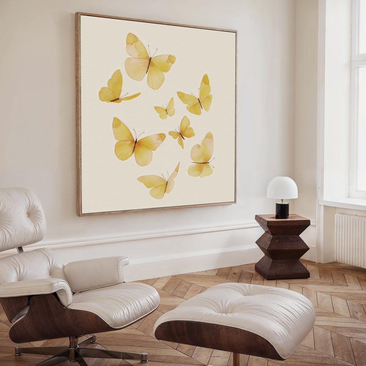 A modern living room with a white lounge chair and ottoman, a geometric wooden side table topped with a round white lamp, and the Butterfly Radiance Canvas Art featuring vibrant yellow butterflies displayed on the wall.