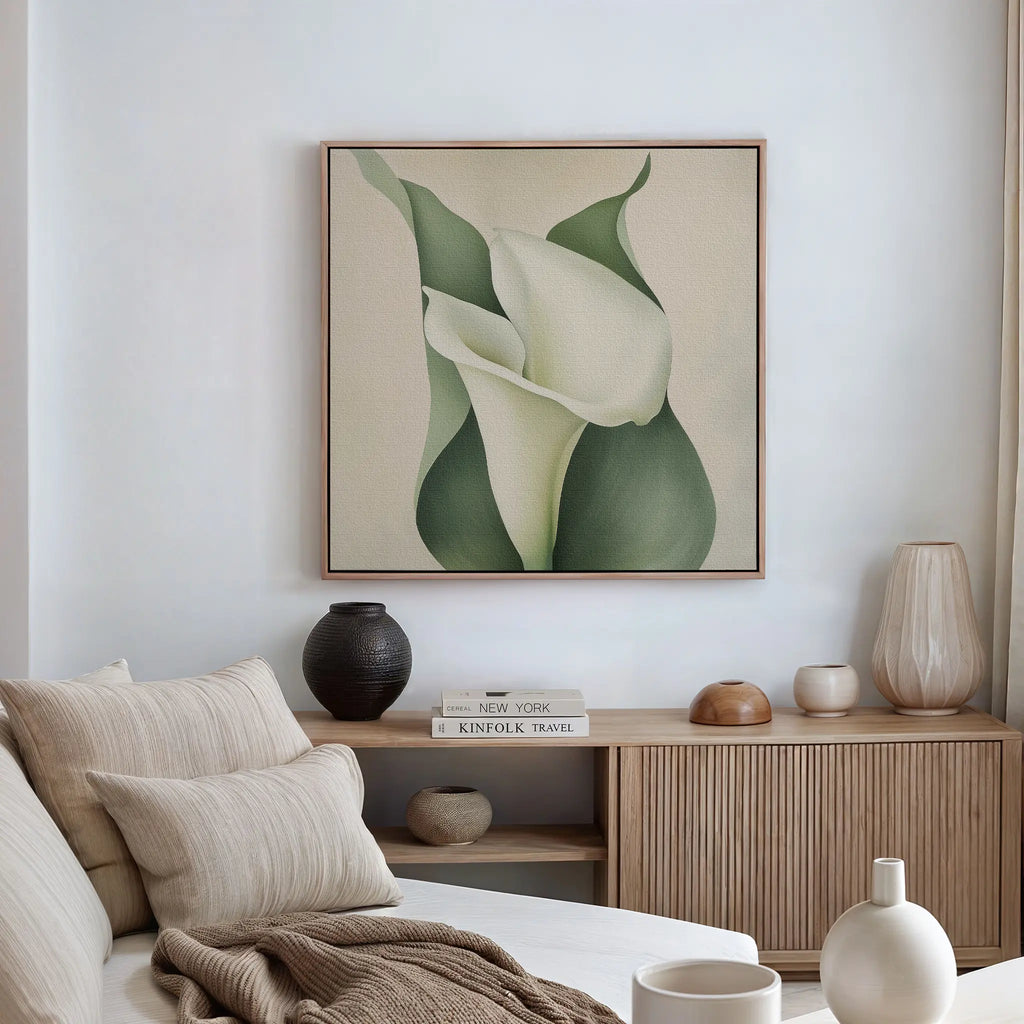 A modern living room with a beige sofa, neutral pillows, and a wooden sideboard. The Calla Duo Canvas Art featuring white calla lilies with green leaves hangs above, complemented by decorative vases and books on the sideboard.