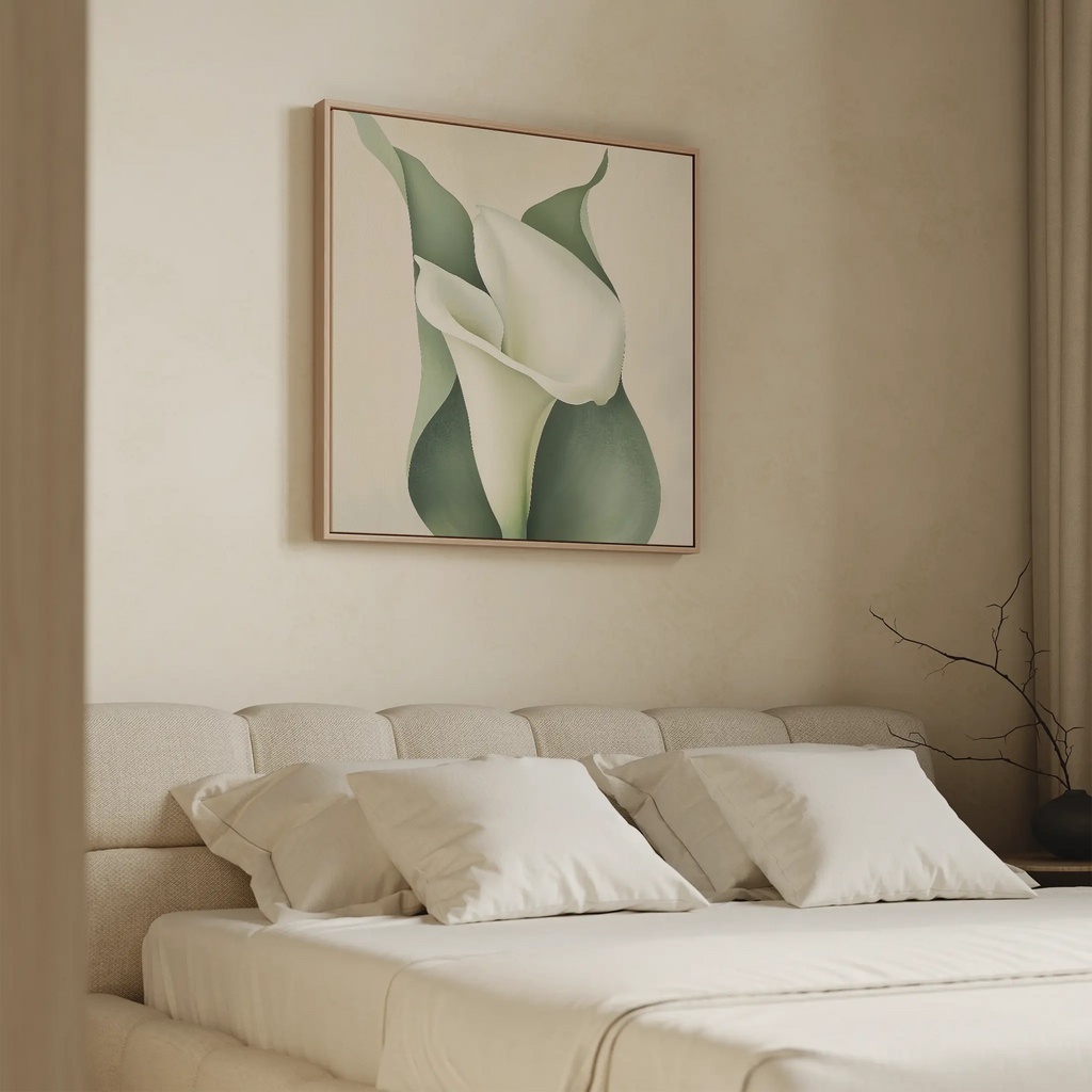 A minimalist bedroom with a beige upholstered bed and white bedding features the Calla Duo Canvas Art above the bed, showcasing green leaves and white flowers. A bare branch on the nightstand completes the modern look.
