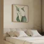 A minimalist bedroom with a beige upholstered bed and white bedding features the Calla Duo Canvas Art above the bed, showcasing green leaves and white flowers. A bare branch on the nightstand completes the modern look.