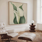 A modern living room with a white leather lounge chair and ottoman, a wooden side table with a white lamp, and the Calla Duo Canvas Art featuring a large white flower with green leaves on the wall.