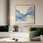 A modern living room features a green armchair, marble accents, and the Calm Swell Canvas Art—a large abstract wall print of flowing blue waves—above a shelf with a vase and books, creating stylish and serene décor.