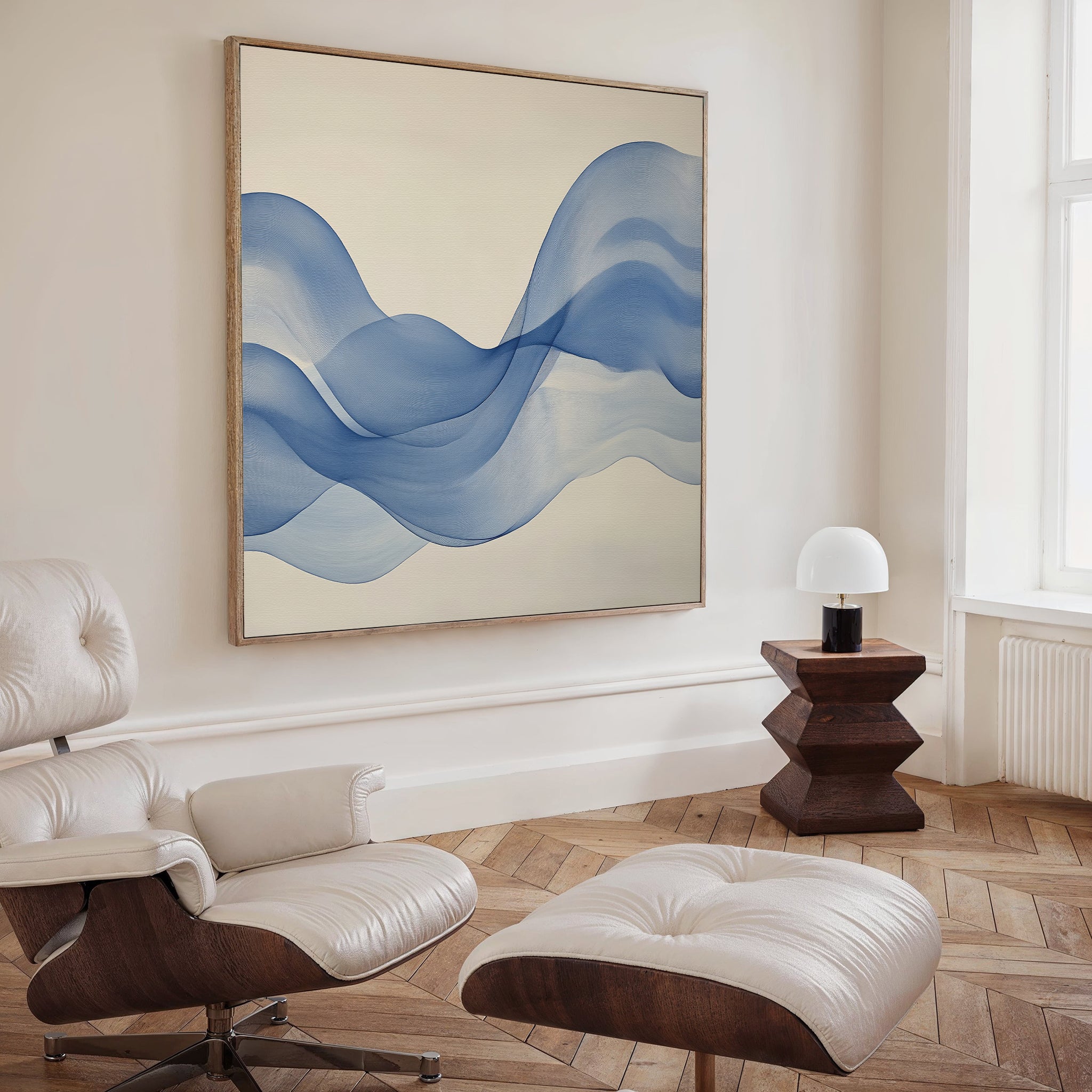A modern living room features a white leather lounge chair and ottoman, a wooden side table with a white lamp, and the Calm Swell Canvas Art with blue wave-like shapes for a stylish decor accent.