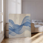 The Calm Swell Canvas Art leans against a white wall, bringing stylish decor to a bright living room with wooden parquet floors, a white sofa, and sunlight streaming through tall windows.