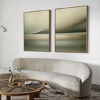 A modern living room with a curved beige sofa, round wooden coffee table, open book, and two large abstract landscape paintings above—featuring the Calm Waterscape Set of 2 for a stylish, tranquil touch.