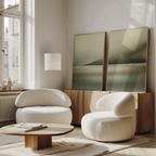 A modern living room featuring two rounded white armchairs, a low wooden coffee table with books, a wooden sideboard, the Calm Waterscape Set of 2 abstract paintings, and a tall window letting in natural light.
