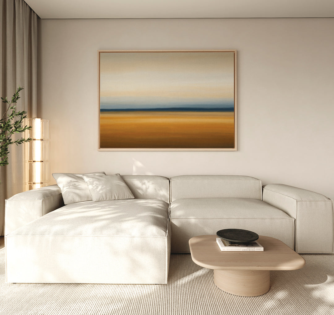A modern living room with a light beige sectional sofa, low wooden coffee table, black bowl, tall lamp, potted plant, and Caramel Plains Canvas Art – Horizontal on the wall in earth tones.