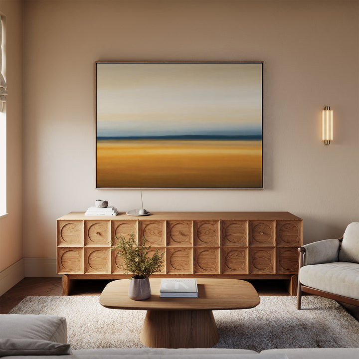 A modern living room with a beige sofa, wooden coffee table, and geometric wooden sideboard. Above the sideboard hangs the Caramel Plains Canvas Art – Horizontal. A soft rug and small plants complete this inviting setting.