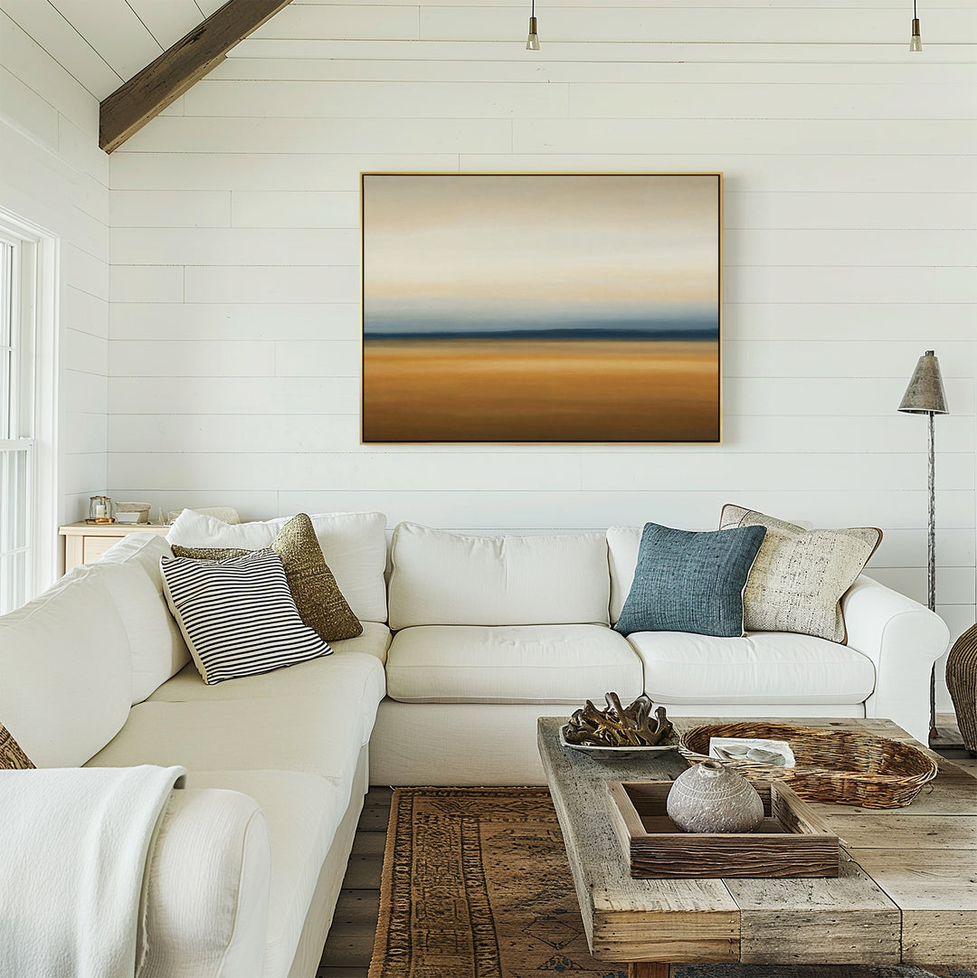 A bright, cozy living room with white shiplap walls, a large beige sectional sofa with assorted pillows, a rustic wooden coffee table, and Caramel Plains Canvas Art – Horizontal displayed on the wall.