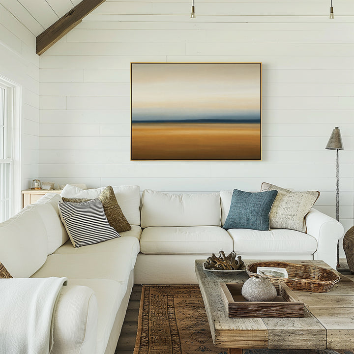 A bright, cozy living room with white shiplap walls, a large beige sectional sofa with assorted pillows, a rustic wooden coffee table, and Caramel Plains Canvas Art – Horizontal displayed on the wall.