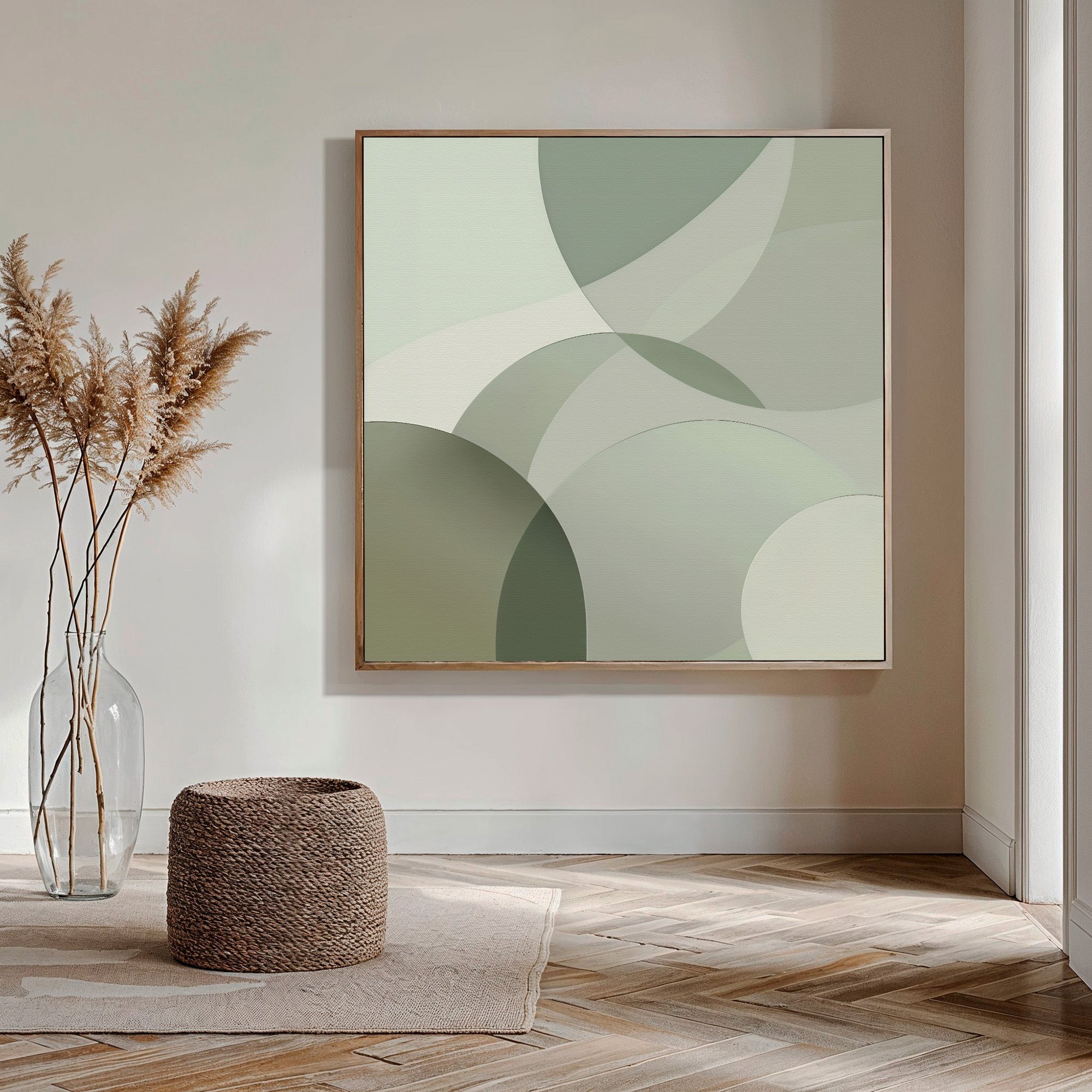 A minimalist living space with Circular Quiet Abstract Canvas Art in soft green on the wall, a glass vase holding dried pampas grass, and a woven pouf placed on a herringbone wood floor.